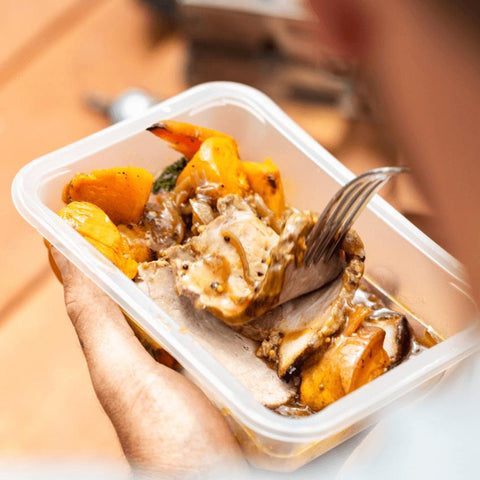 Hand holding container with roast pork & vegetables