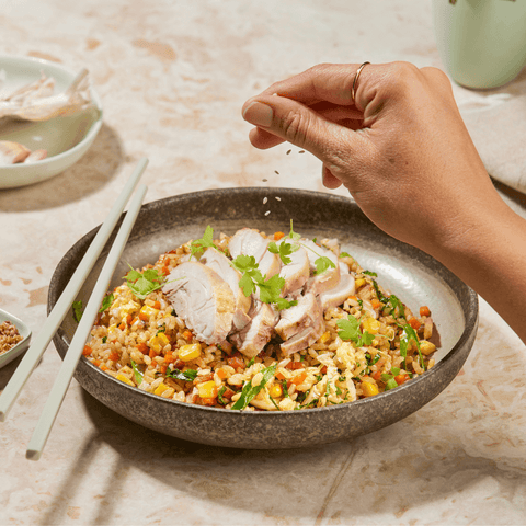 Bowl of fried rice with chicken, hand over top sprinkling sesame seeds