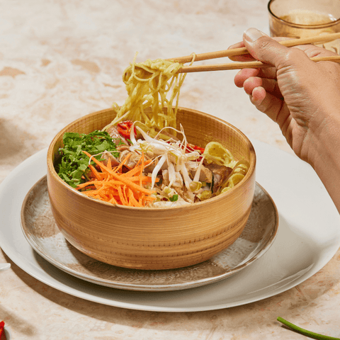 Bowl of laksa, hand holding chop sticks picking up noodles