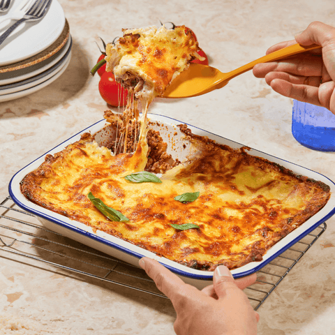 Family sized lasagna, hand holding spatula lifting slice with stringy cheese