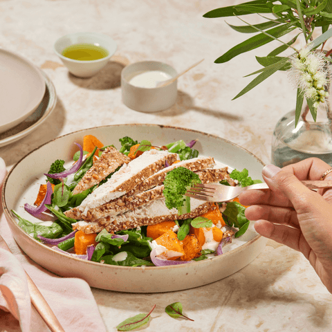 Dukkah Chicken Salad on a plate. Hand holding fork with broccoli on it